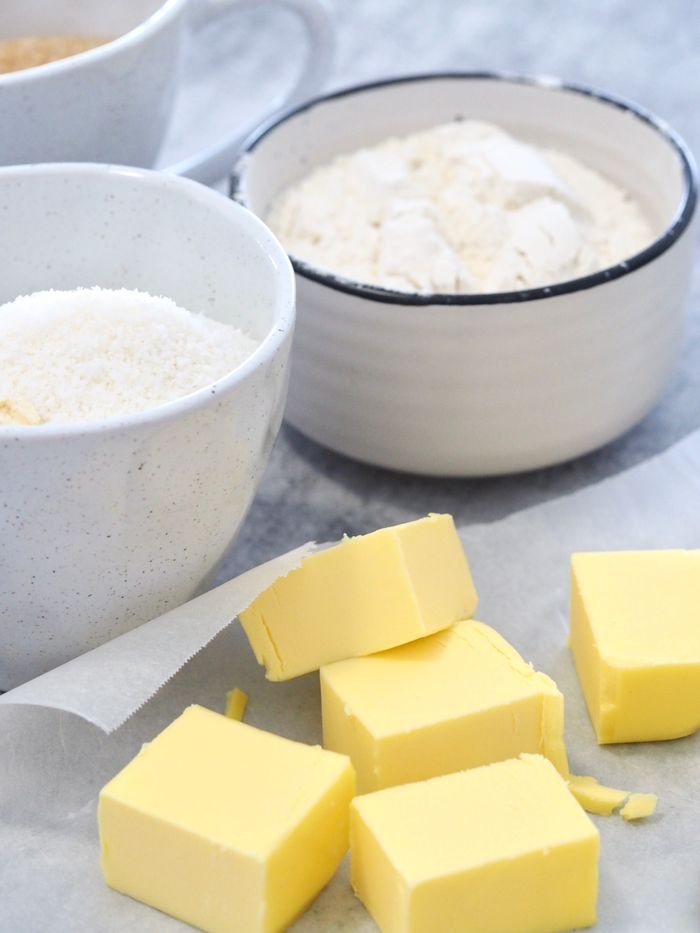 Butter cubes and flour in bowls on a marble counter for baking preparation.